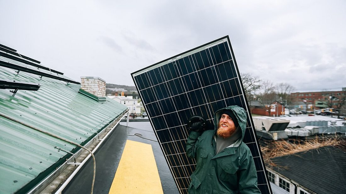 Technician carrying a solar module on a roof, illustrating DCR and ALMM compliant panels for rooftop solar installation
