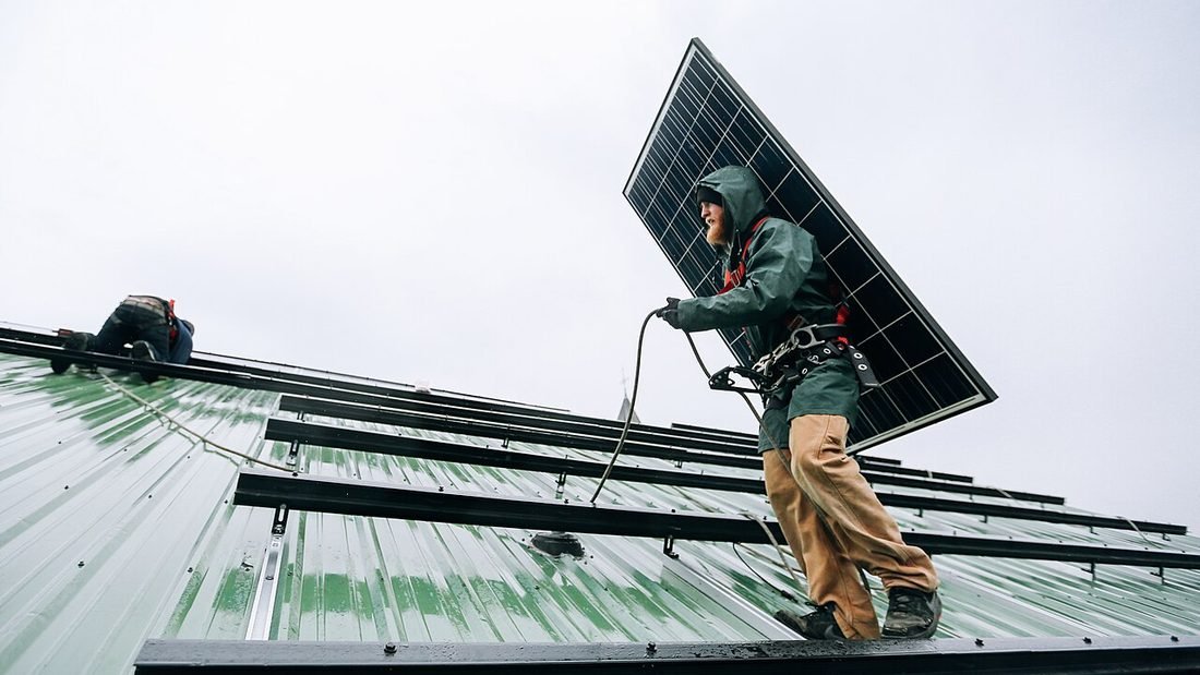 Technician carrying a solar panel across a roof during installation by a solar company
